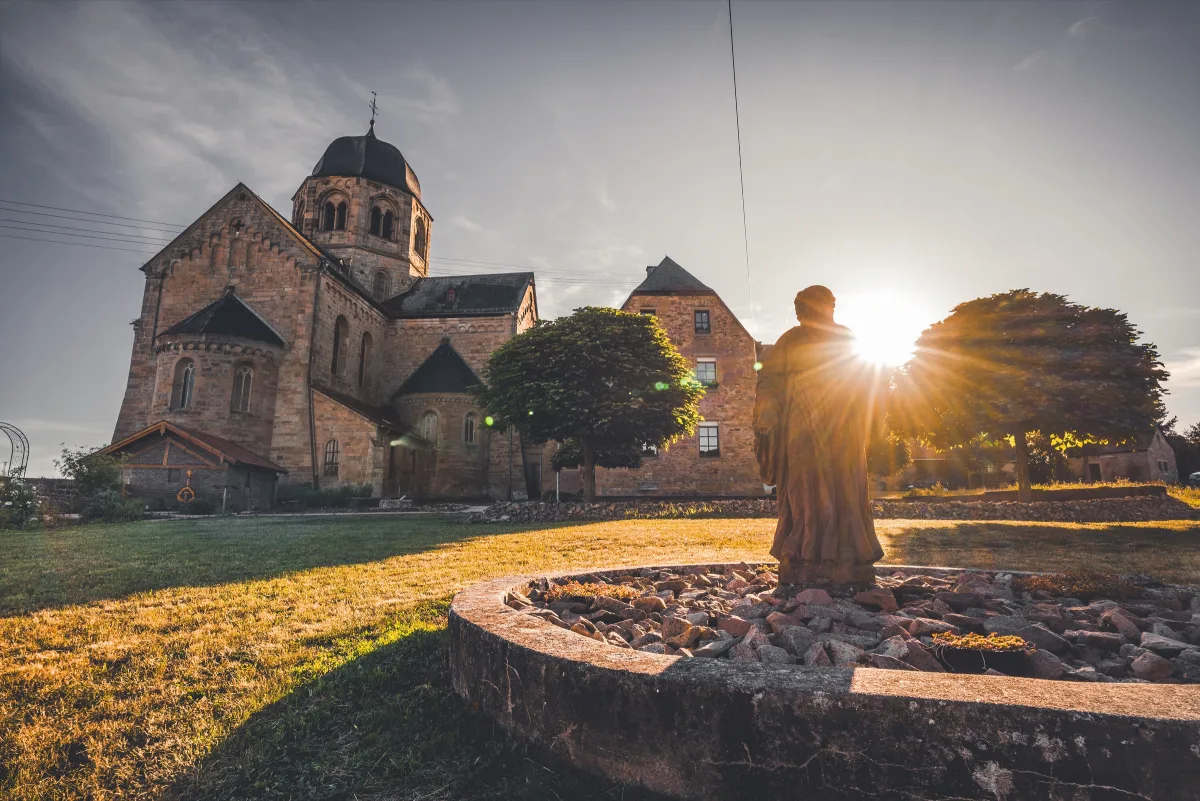 Klosterkirche Sponheim im Gegenlicht der Abendsonne mit M&ouml;nchsstatue im Vordergrund