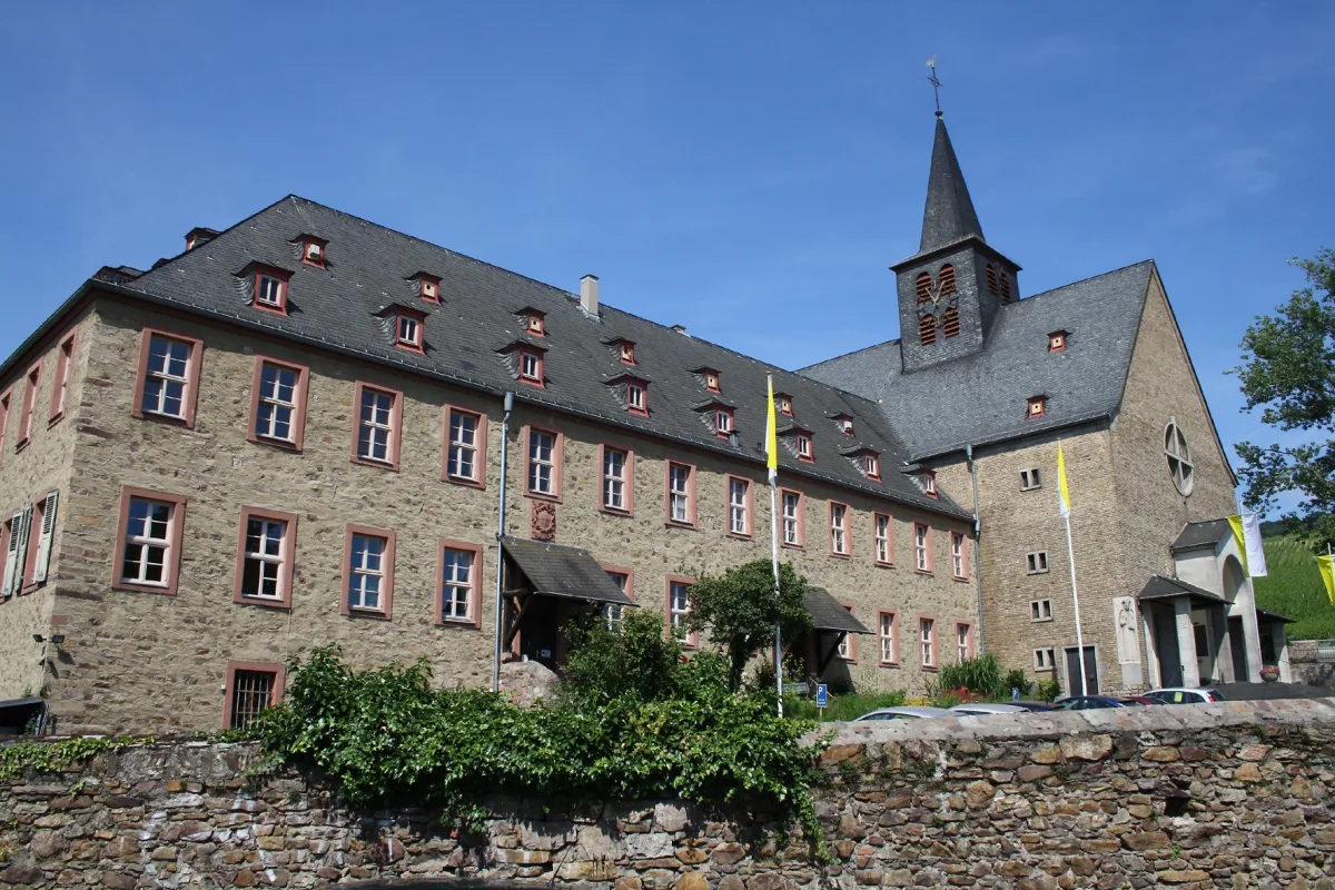 Pfarr- und Wallfahrtskirche St. Hildegard in Eibingen mit Bruchsteinfassade, Dachreiter und gelb-wei&szlig;en Kirchenfahnen vor blauem Himmel