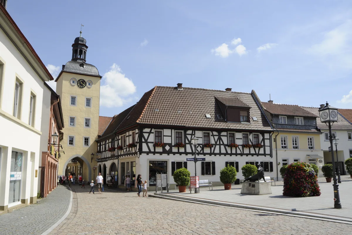 R&ouml;merplatz in Kirchheimbolanden mit dem gelben Rathausturm, einem Fachwerkhaus und Passanten auf dem gepflasterten Platz