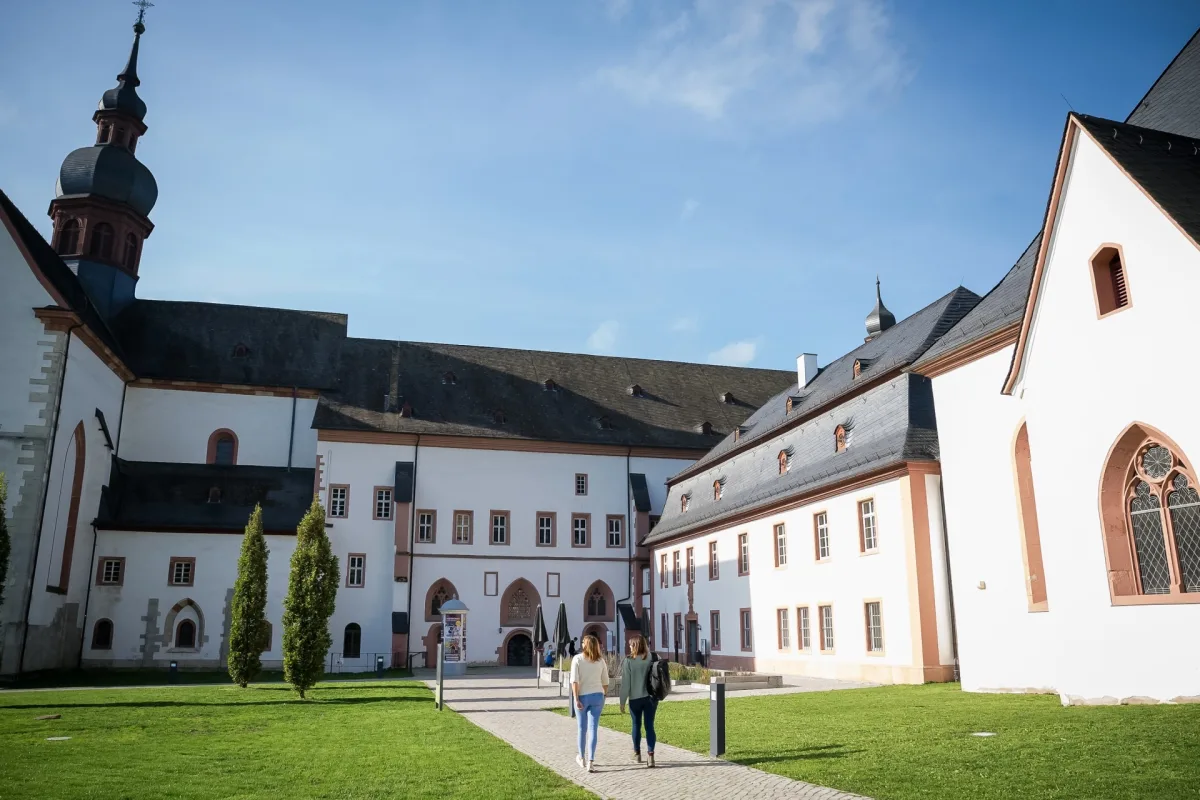 Innenhof von Kloster Eberbach mit Basilika und wei&szlig;en Klostergeb&auml;uden, zwei Besucherinnen auf dem gepflasterten Weg