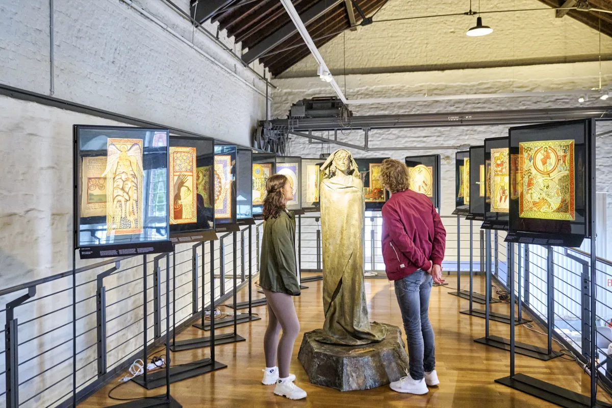Besucher betrachten die bronzene Hildegard-Statue und beleuchtete Tafeln mit mittelalterlichen Miniaturen im Museum am Strom